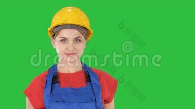 微笑的建筑工人妇女站着变换姿势，双手折叠，双手放在臀部，双手放在绿色的口袋里